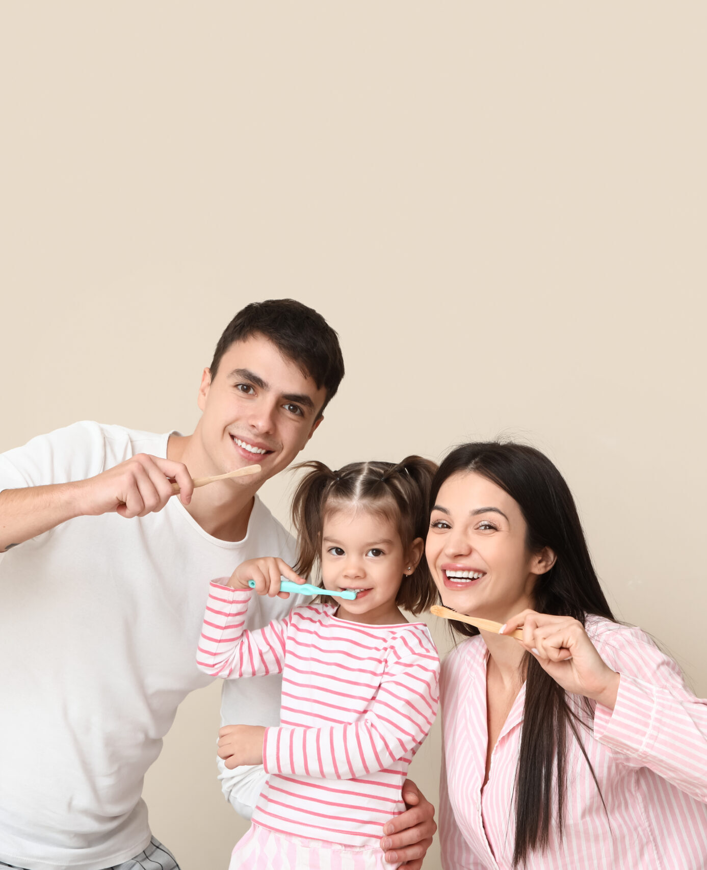 Happy family with cute little daughter brushing teeth on beige background