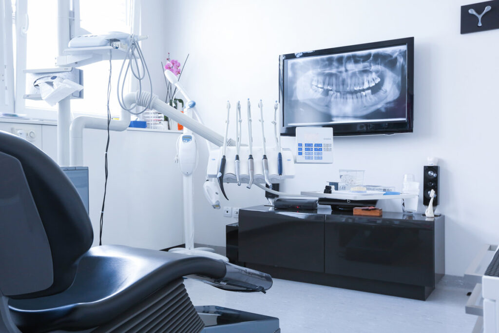 Dentists chair and tools with x-ray picture on TV in the background. Dental care, dental hygiene, checkup and therapy concept.