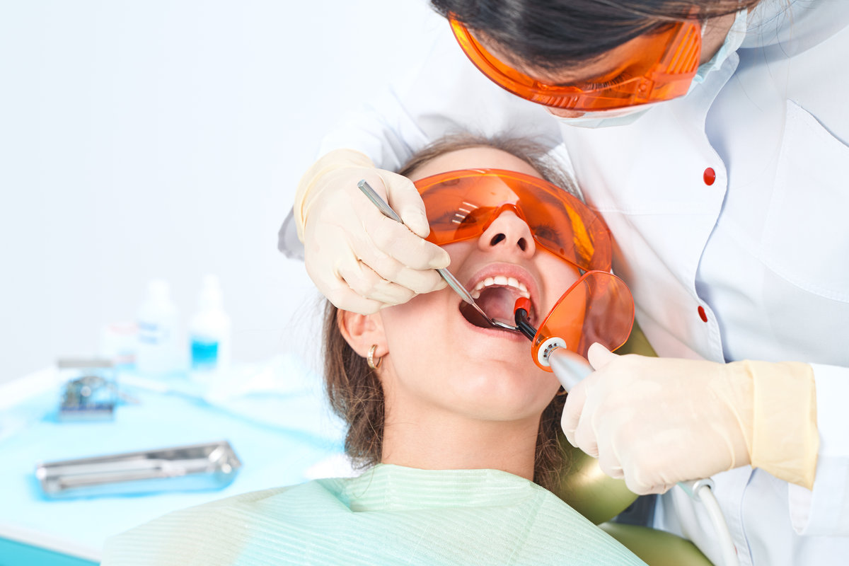 Girl at the doctor. Dentist places a filling on a tooth with dental polymerization lamp in oral cavity. over clinic background.