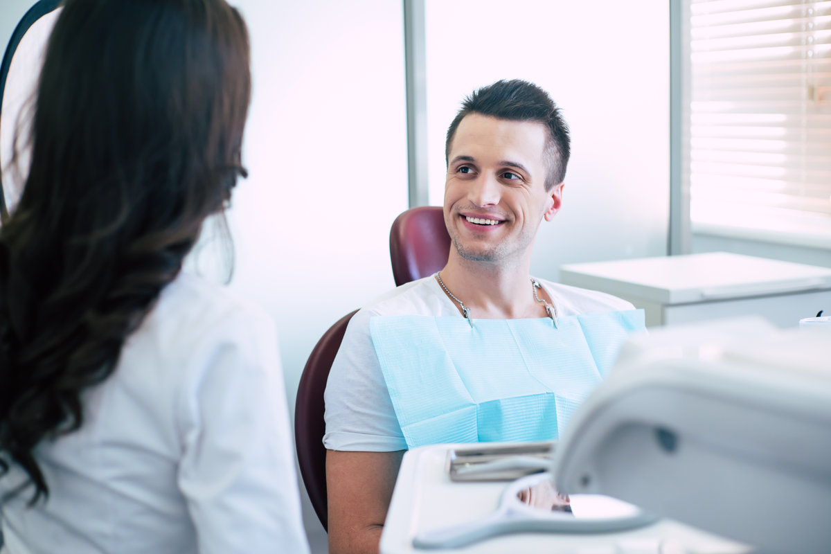 Talk turkey. A conversation between dentist and a patient who is sitting in the dental chair in front of white wall and bright lighted window and smiling because of great work of the doctor.